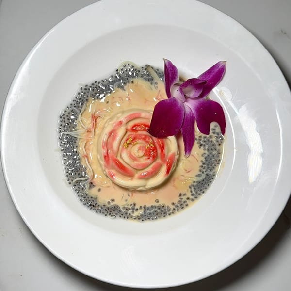 Indian dessert with a rose-shaped cream, red syrup, basil seeds, and a purple orchid.