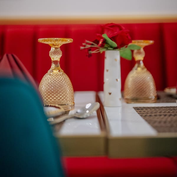Elegant table setting with ornate golden glasses, a white vase with red roses, and silverware.