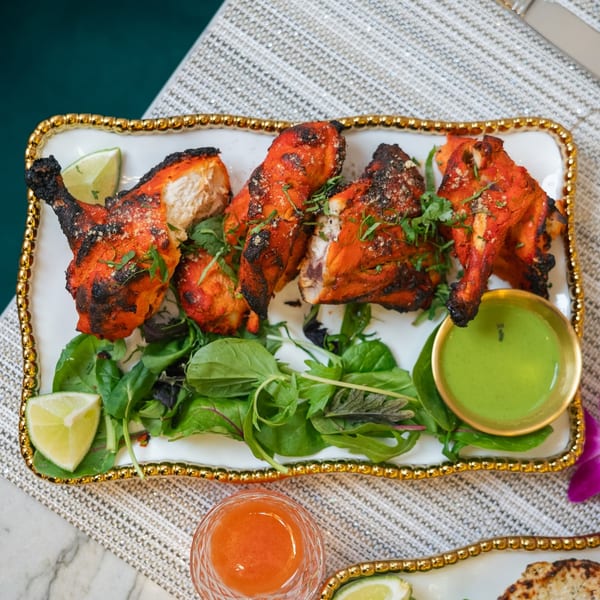 Red Chilli's Tandoori Chicken, garnished with cilantro, lime, and served with green chutney.