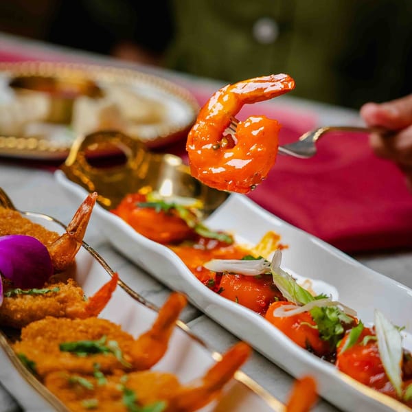 A fork lifts a vibrant orange shrimp from a dish of Indian appetizers at Red Chilli.