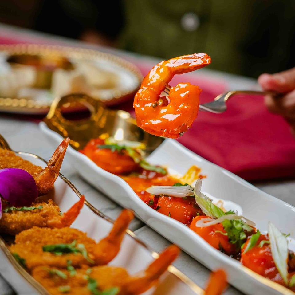 A fork lifts a vibrant orange shrimp from a dish of Indian appetizers at Red Chilli.