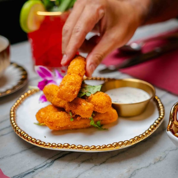 Hand reaching for crispy fried paneer sticks with dipping sauce and a cocktail at Red Chilli.
