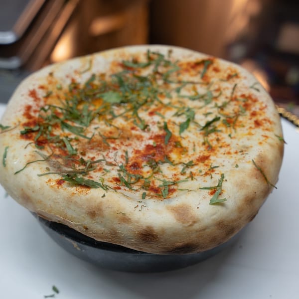 Indian bread, likely naan, topped with red spice and green herbs, served in a black bowl.