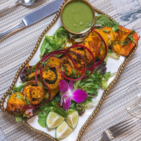 Indian chicken tikka with green chutney, lime wedges, and a purple orchid on a white platter.