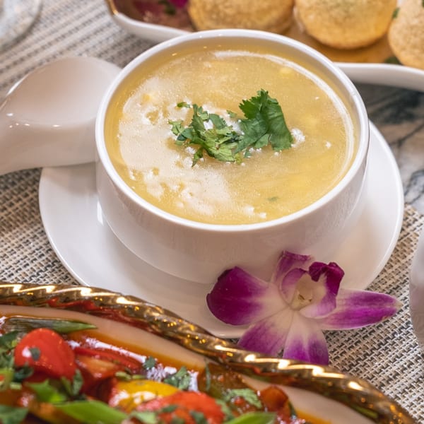 A bowl of Indian soup with cilantro, a purple orchid, and a dish of vegetables.