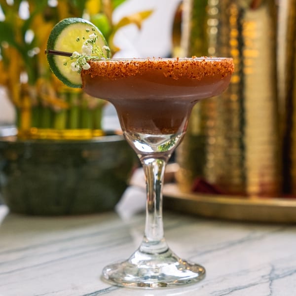 A Red Chilli cocktail in a margarita glass, garnished with a lime slice and small white flowers.