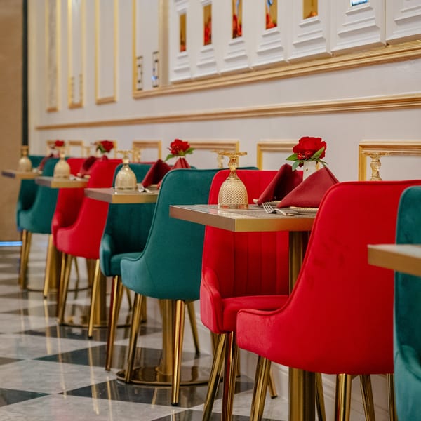 Restaurant interior with rows of red and teal velvet chairs, gold tables, and red roses.