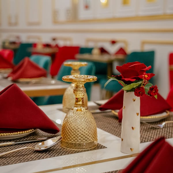 Elegant restaurant table set with red napkins, golden glassware, and a white vase with red roses.