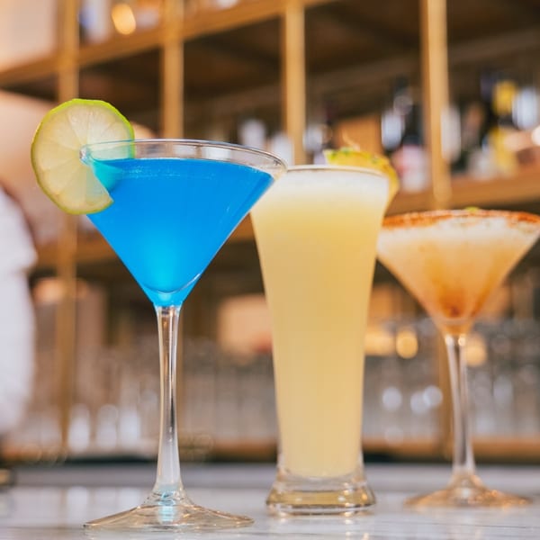 Three colorful cocktails, including a blue martini with lime, on a bar at Red Chilli.